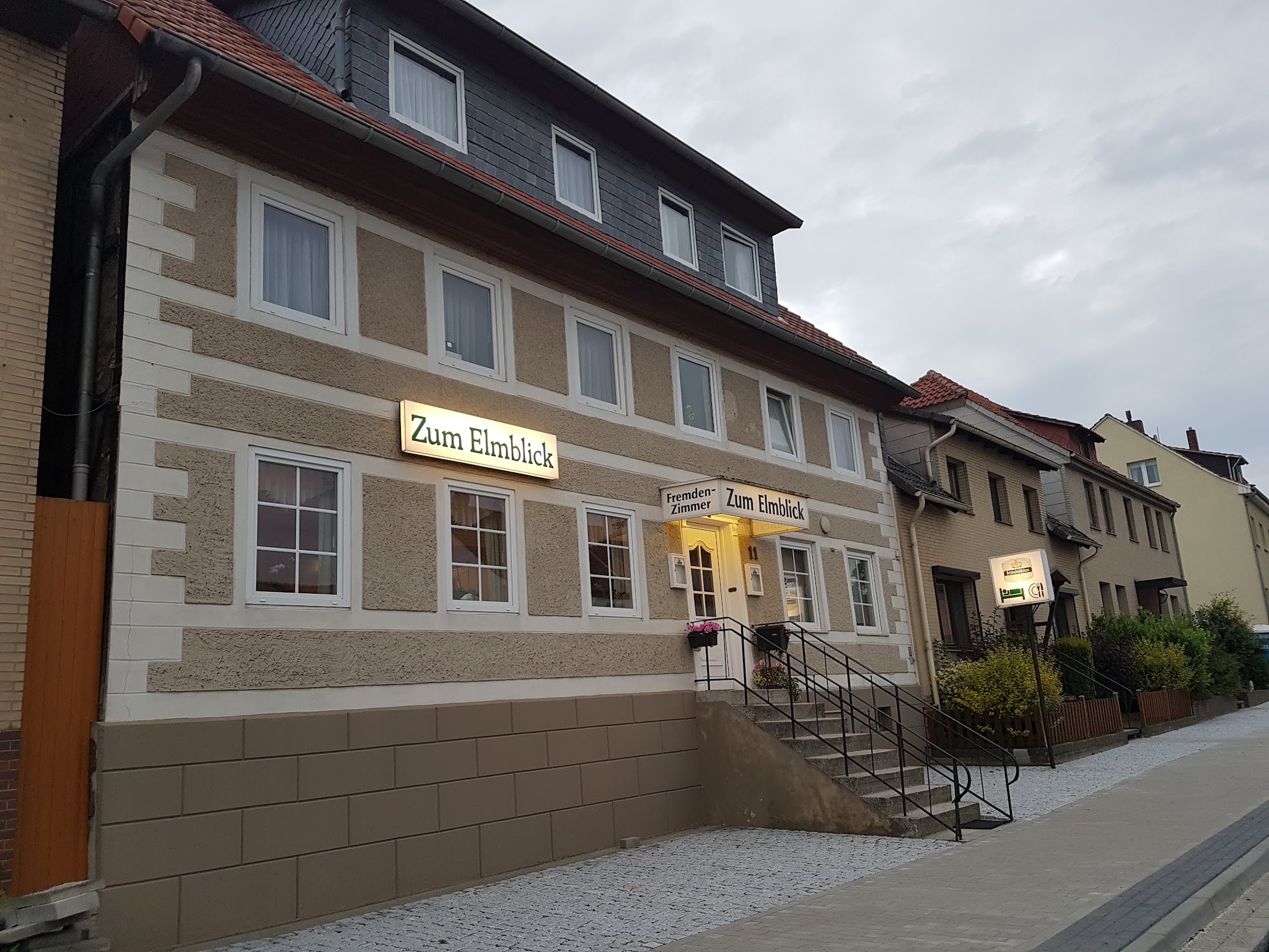 Gasthof Zum Elmblick, Ansicht der Fassade mit beleuchtetem Schild und Fremdenzimmer-Eingang
