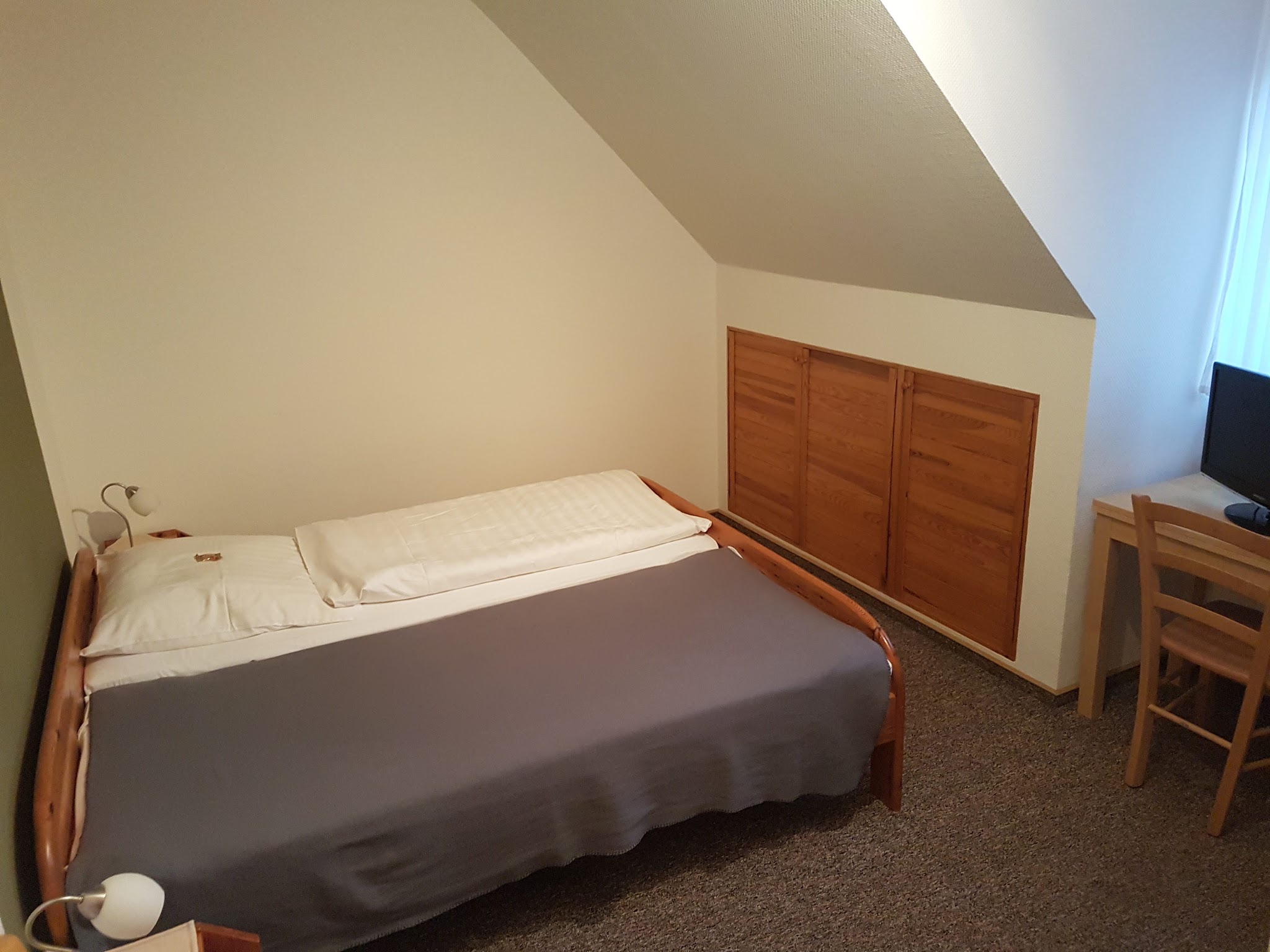 Fremdenzimmer im Gasthof Zum Elmblick mit Bett, Schrank und Fernseher unter der Dachschräge